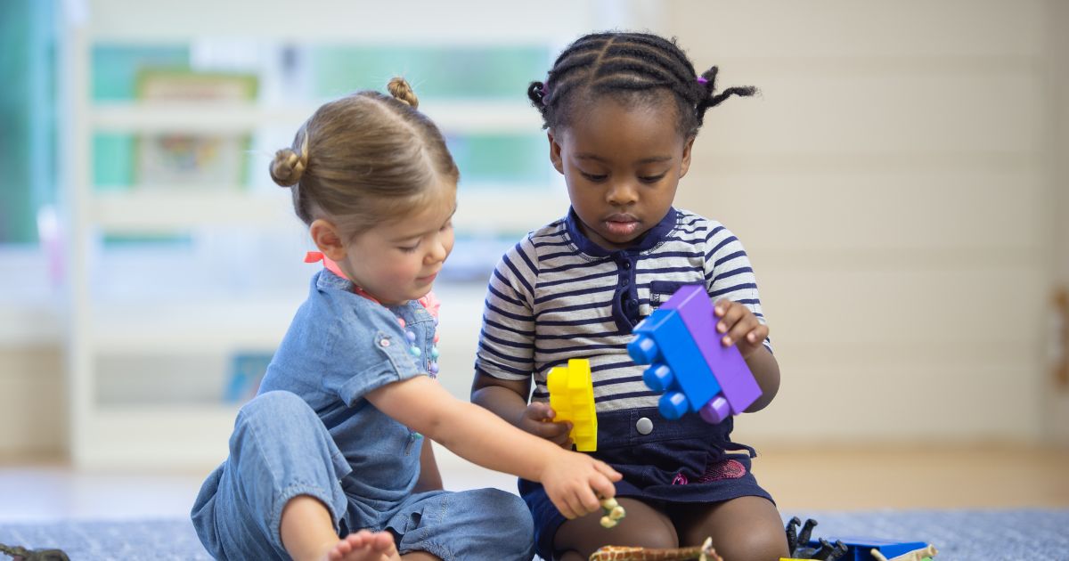 zwei Kinder, die auf dem Boden sitzen und mit Bauklötzen spielen