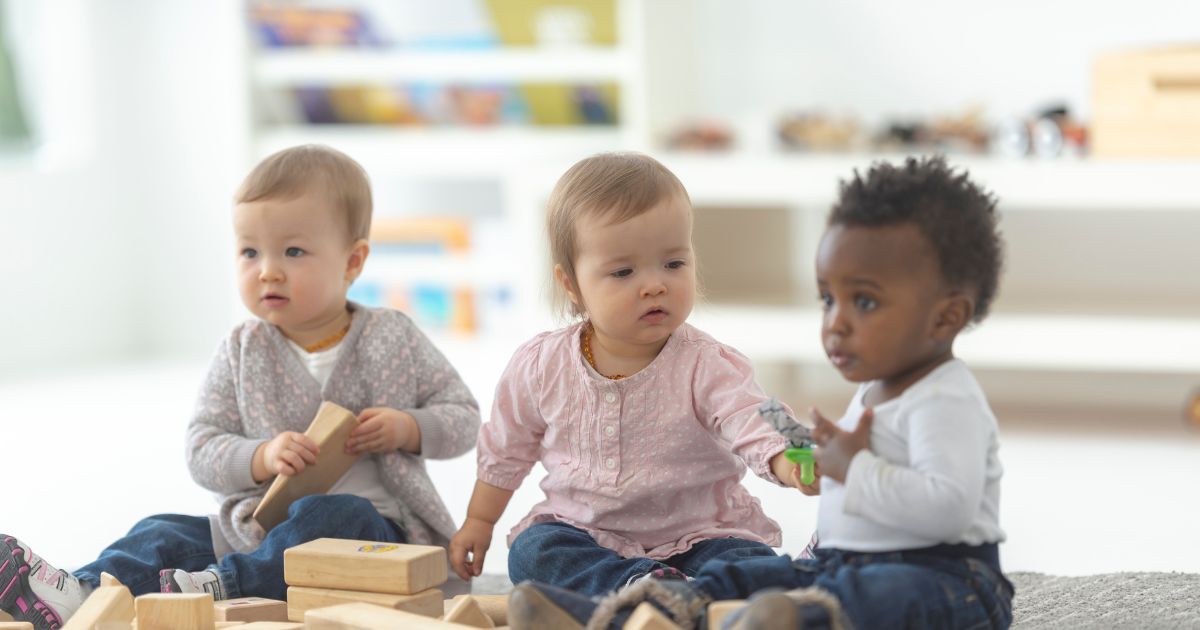 Drei Kleinkinder sitzen auf dem Boden und spielen mit Bauklötzen