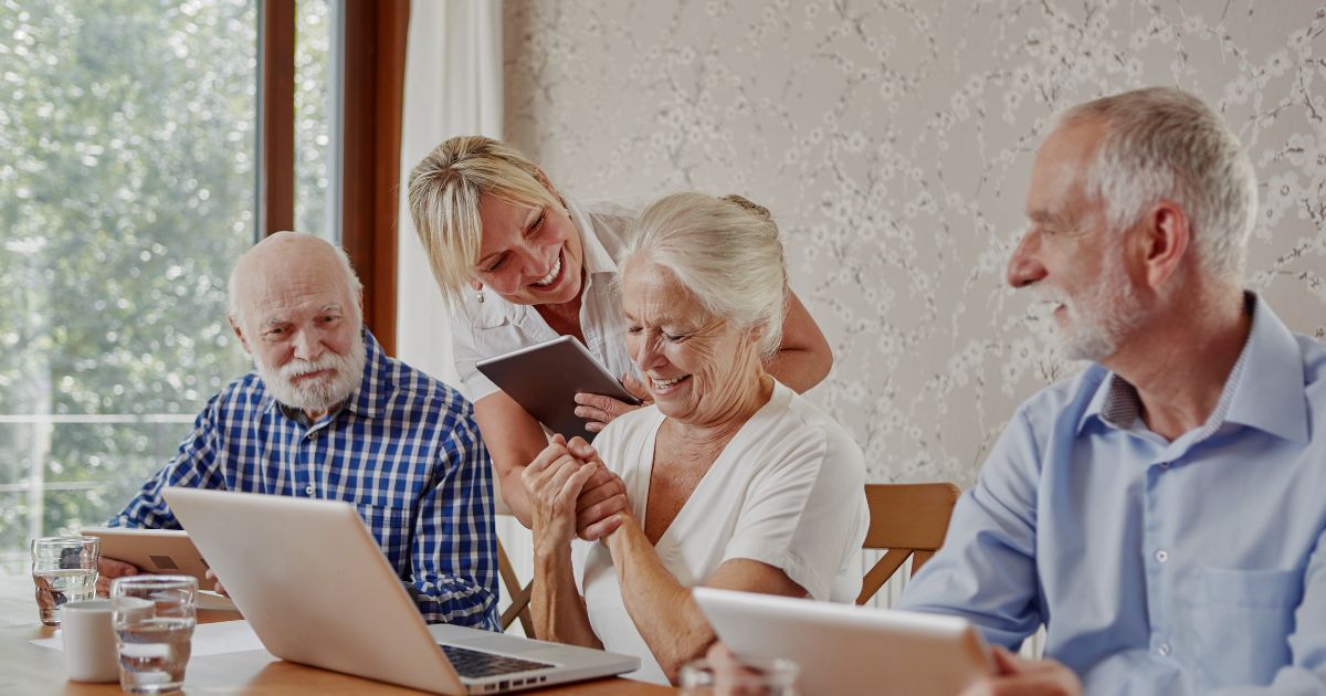 Drei Senior:innen an Laptops und eine Kursleitung, die Dinge erklärt.