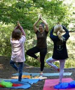 Svenja Dridiger zeigt die Yogapose "Baum"; zwei Kinder machen mit.
