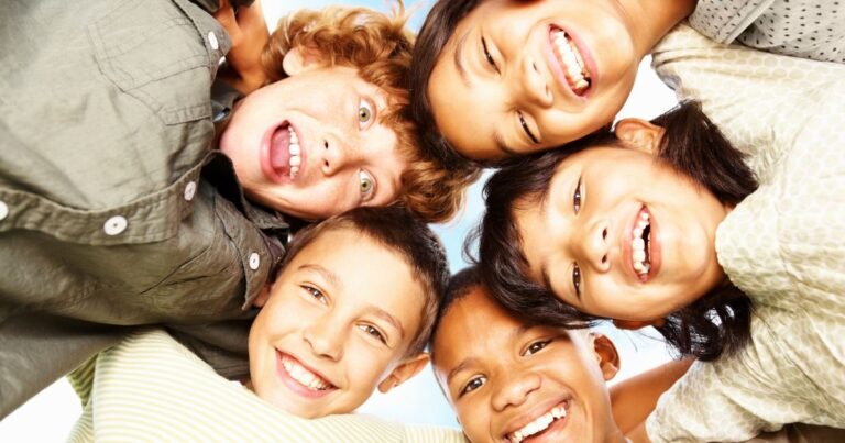 Vier Schulkinder stecken ihre Köpfe zusammen und lachen von oben in die Kamera