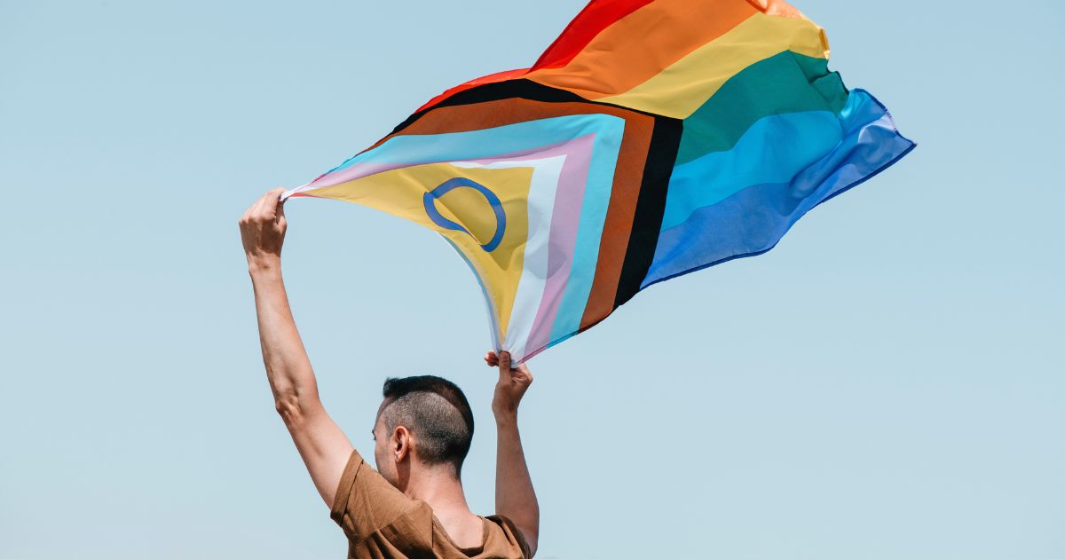 Männlich gelesene Person hält LGBTQIAN+ Flagge hoch