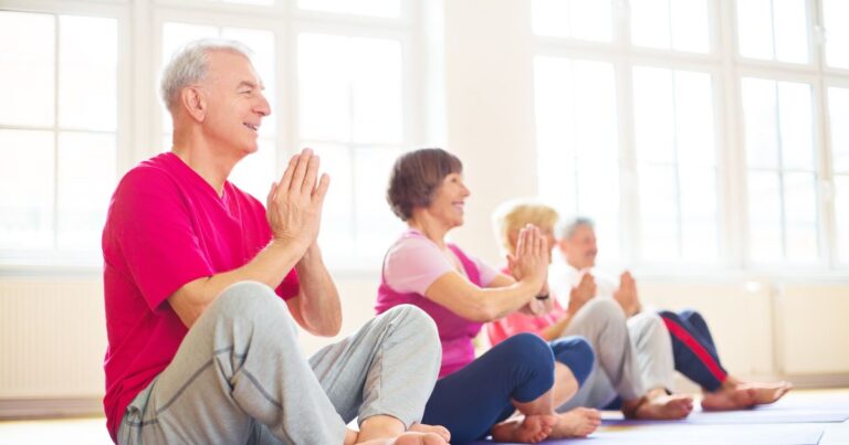 Vier ältere Personen, die in einem hellen Raum sitzend Yoga machen