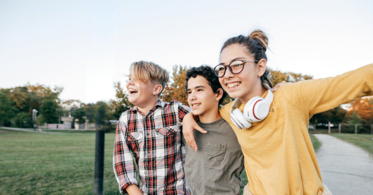 3 Jugendliche gehen Arm in Arm durch einen Park und sehen freudig aus.