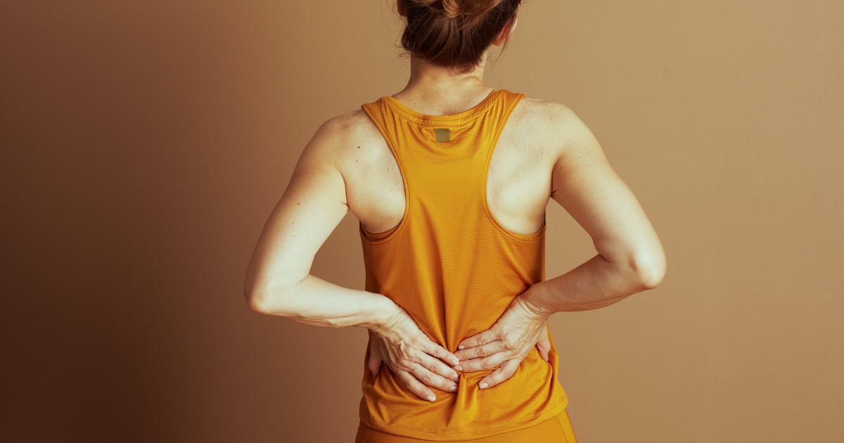 Weiblich gelesene Person von hinten, die sich am unteren Rücken anfasst.