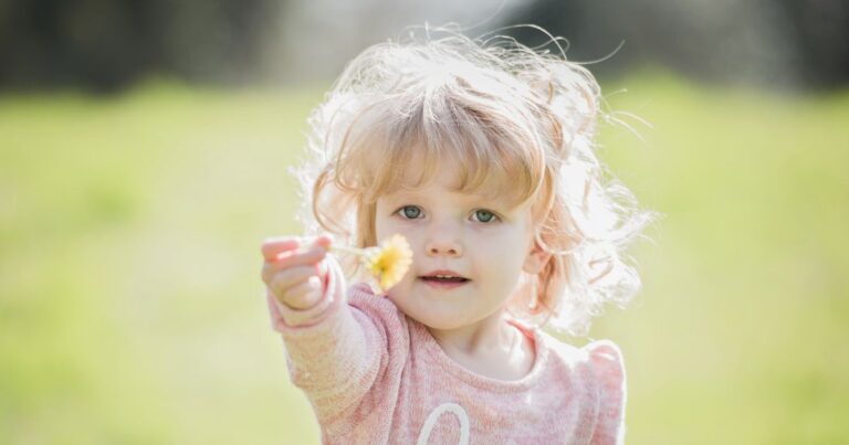 Kleinkind streckt Hand aus und zeigt Gänseblümchen.