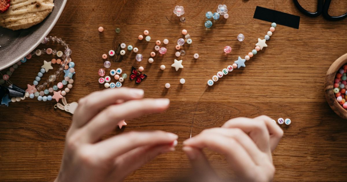 Hände fädeln Perlen auf ein Band auf.