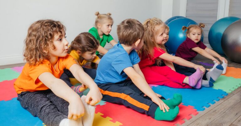 Kinder auf Turnmatten machen Dehnübungen.