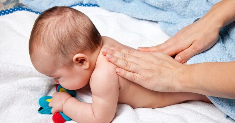Baby liegt auf dem Bauch, Hände streichen über den nackten Rücken.